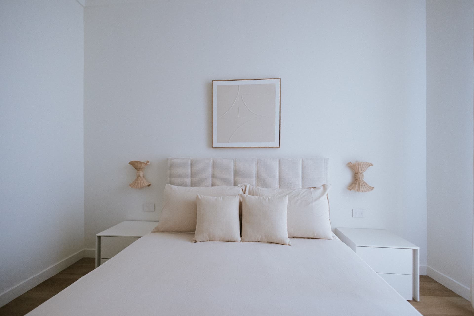 The all-white primary bedroom with woven sconces