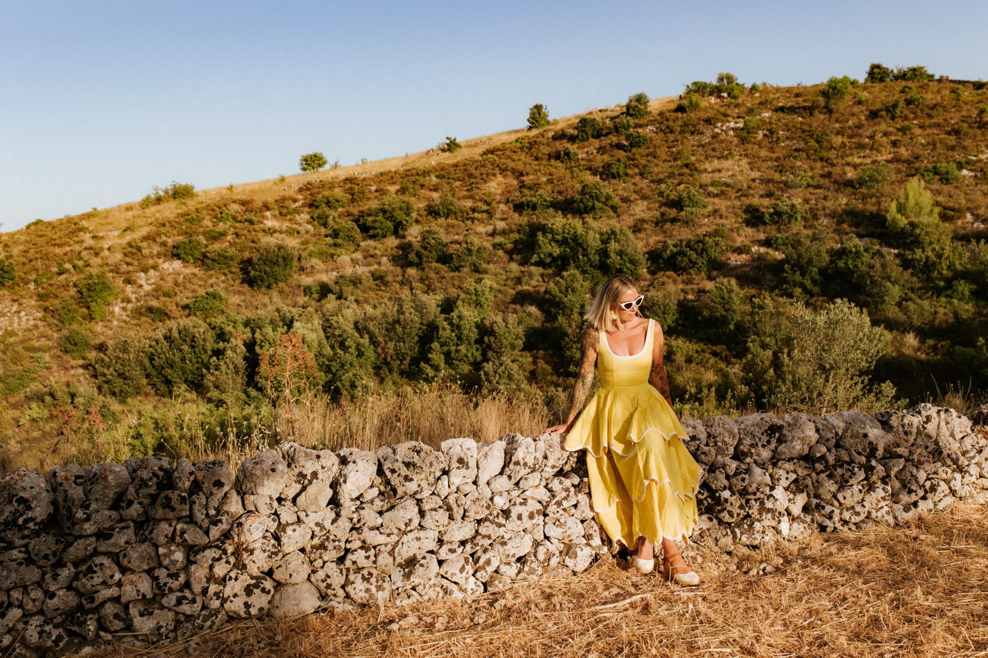 Kat on a hillside of the olive orchard near Noto, seated on a dry-stone wall