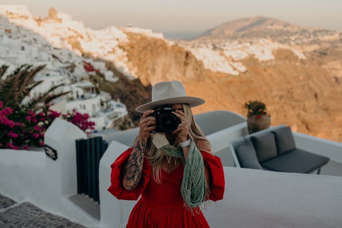 Kat Moore holding a camera to her eye on a terrace above the sea at sunset