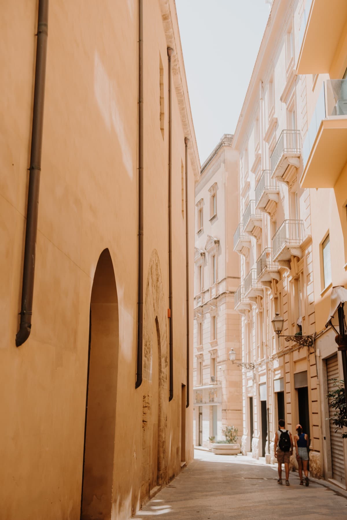 A sunlit alley of ochre buildings in a Sicilian town, edited with the Limone preset