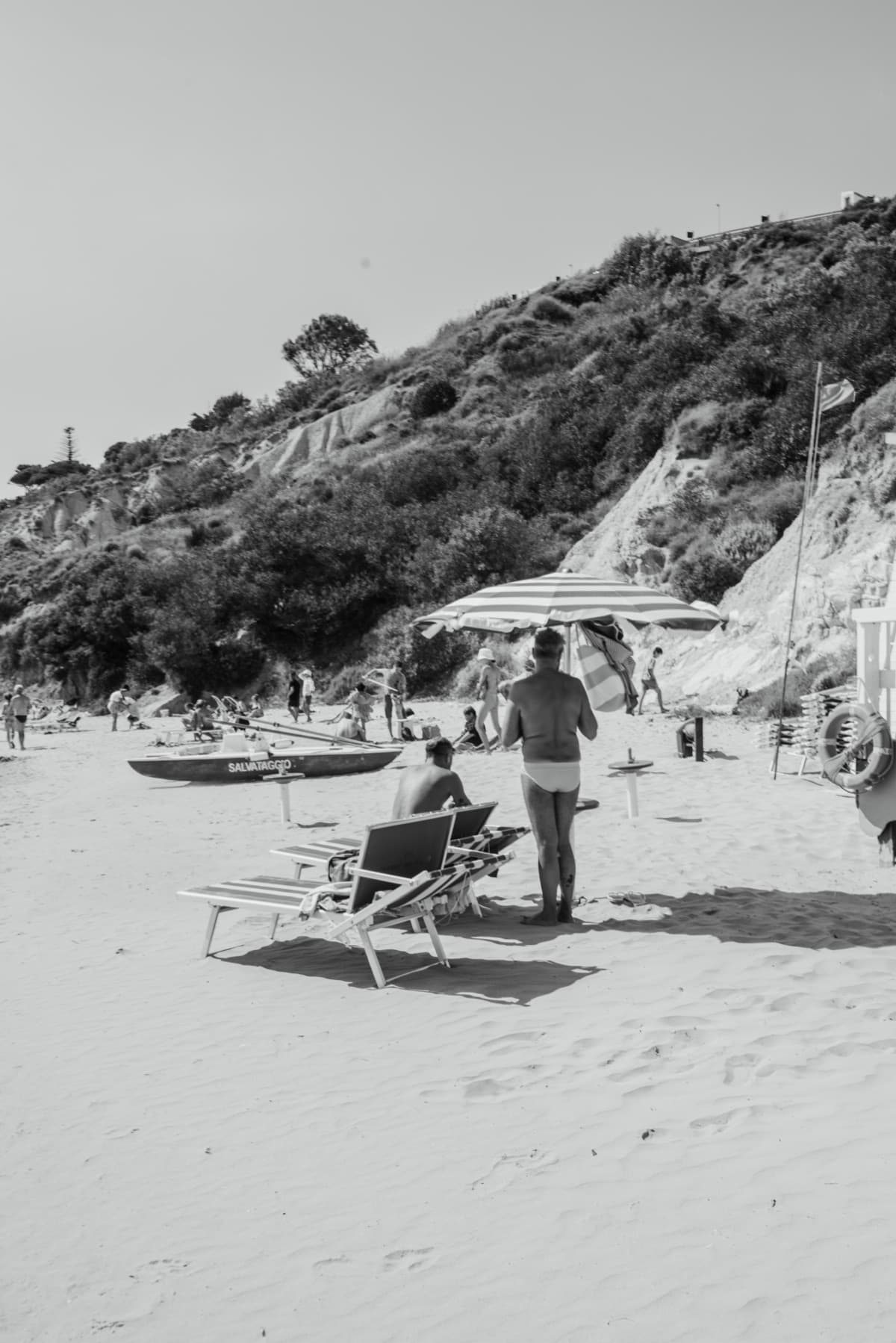 A beach with striped umbrellas below a green headland, edited with the Ombra preset