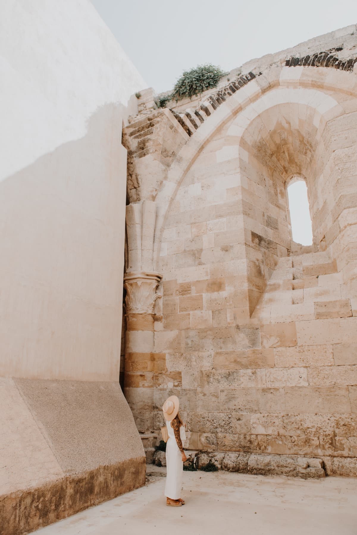 A woman in white beneath a limestone arch in Ortigia, edited with the Pietra preset